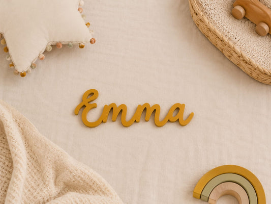 Nombre de madera personalizado Emma en letra ligada color mostaza sobre manta